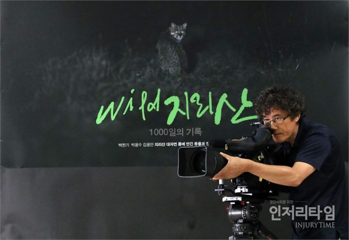 'Wild 지리산-1000일의 기록' 포스터 앞에서 촬영 포즈를 취한 백한기 작가. 사진은 백 사진가가 자동카메라로 직접 찍은 것이다. [백한기 사진가 제공]