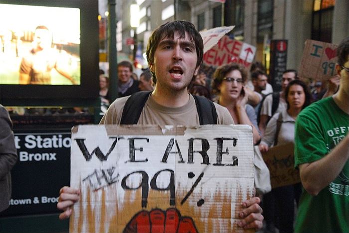 A man is holding a sign that says, "We Are The 99%" at a Occupy Wall Street protest.